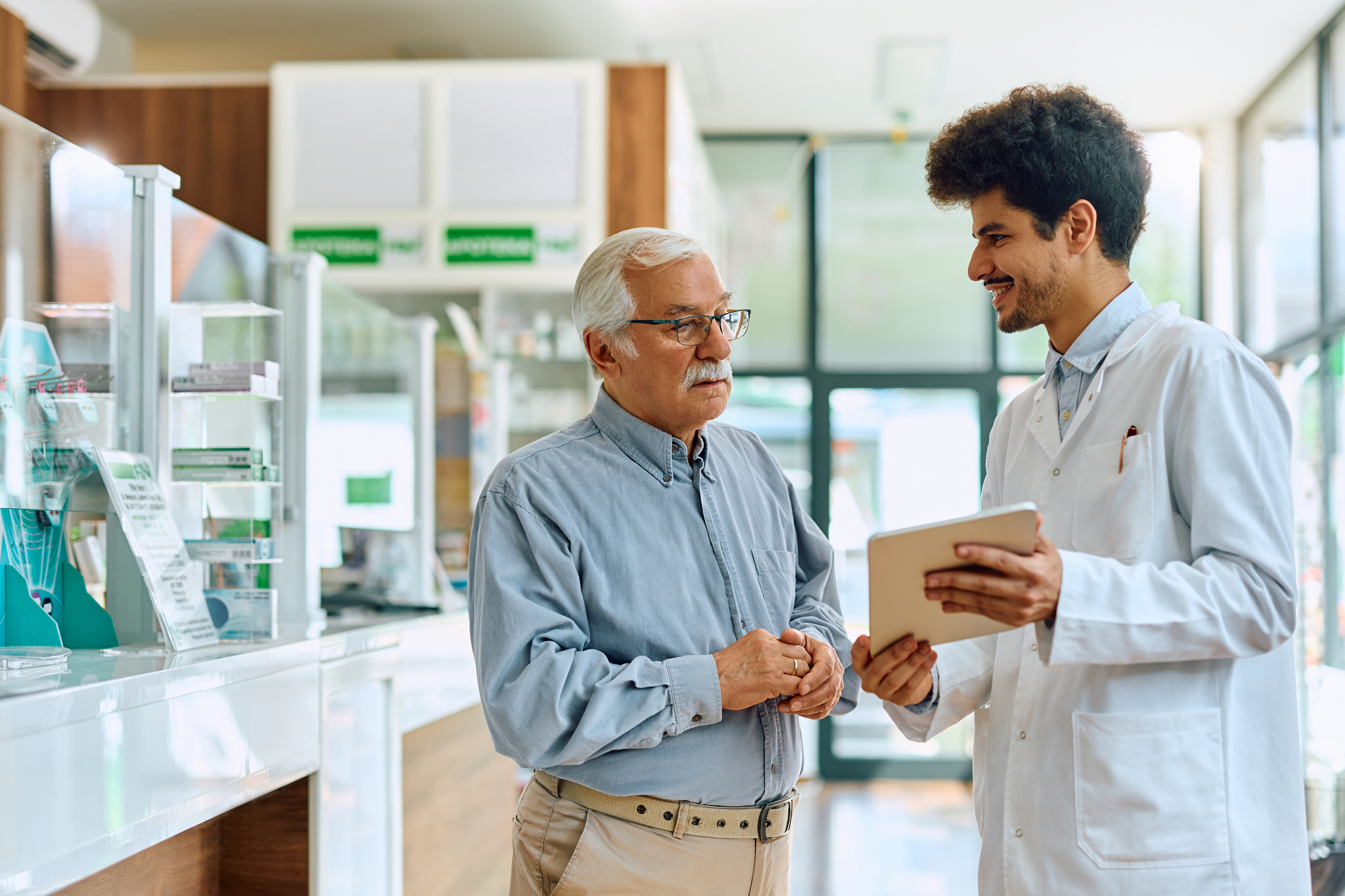 pharmacist and customer in retail pharmacy using digital tablet to show and provide solutions